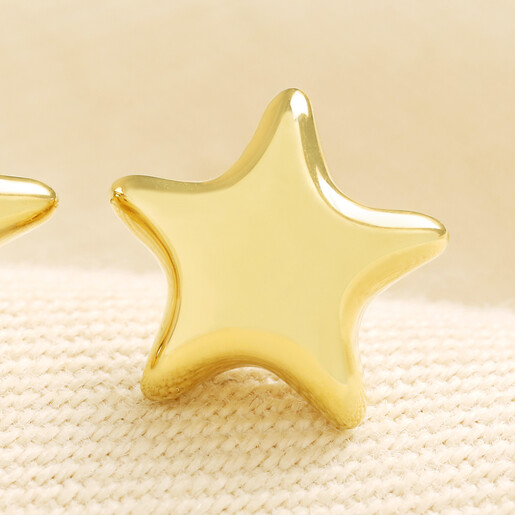 Close up of a polished gold bubble star stud earring on woven fabric