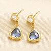 Pair of gold drop earrings with faceted blue triangle glass charms lying flat