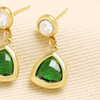 Close-up of gold drop earrings featuring green triangle glass charms on textured fabric