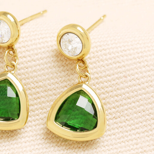 Close-up of gold drop earrings featuring green triangle glass charms on textured fabric