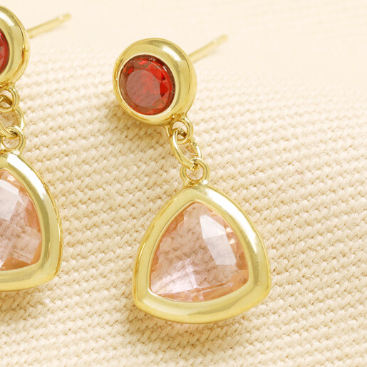 Close-up of gold drop earring with red crystal and pink triangle glass charm