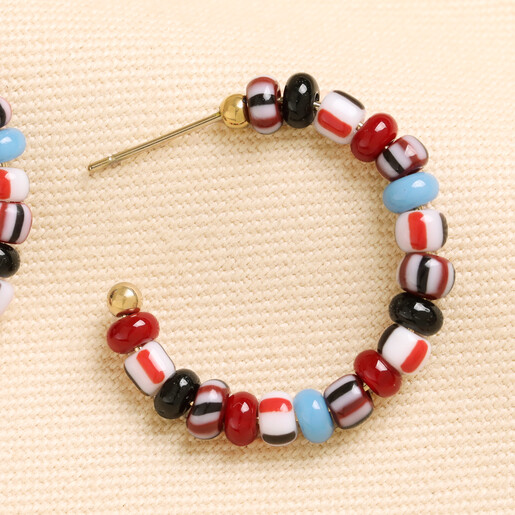 Close up of gold open hoop earring with red and blue glass beads