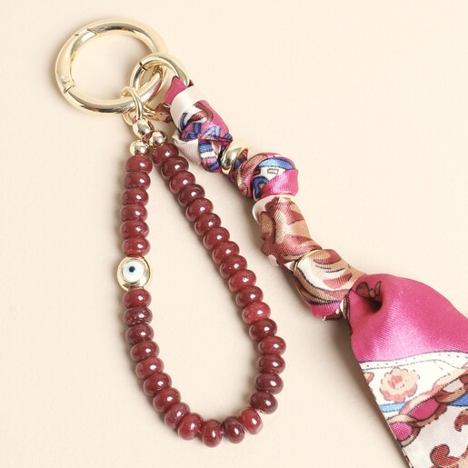 Close-up of red gemstone beads, evil eye charm and silky patterned ribbon on gold clasp