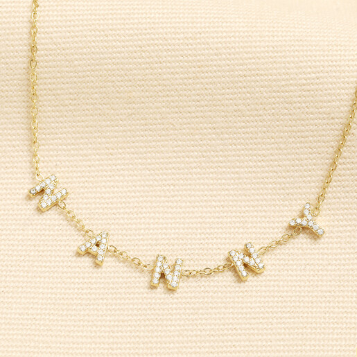 Gold stainless steel chain necklace with crystal charms spelling NANNY on cream background
