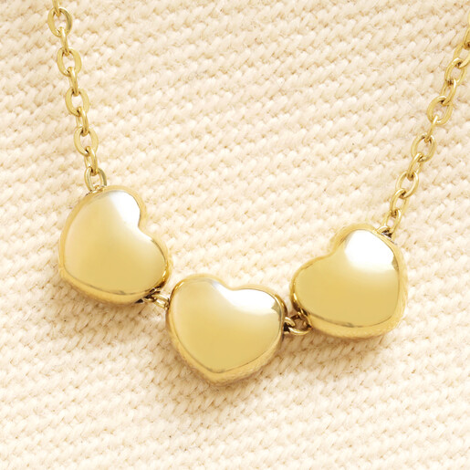 Close-up of three linked polished gold heart charms on a stainless steel chain