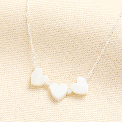 Silver chain necklace with three white heart charms on neutral fabric