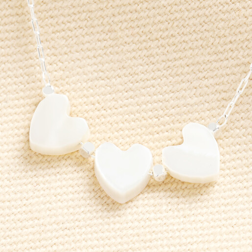 Close up of three white heart charms and silver beads on fine chain