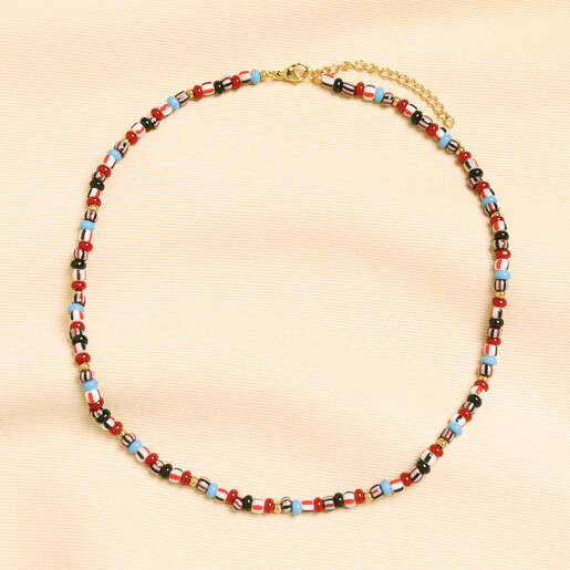 Red and blue glass beaded necklace laid flat in a loop on cream fabric