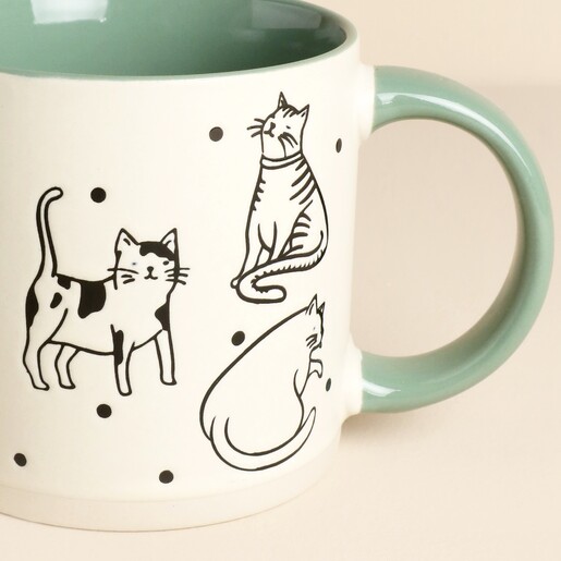 Close up of illustrated black and white cats on a ceramic mug with green handle