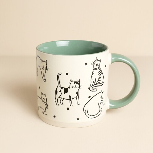 Off white stoneware mug with black cat illustrations and a sage green handle