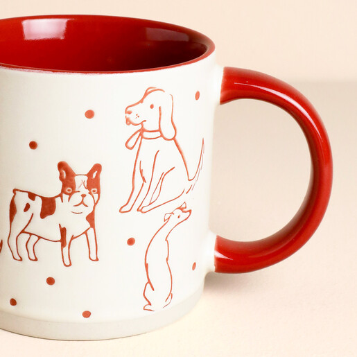 Close-up of red dog illustrations on cream ceramic mug with curved red handle.