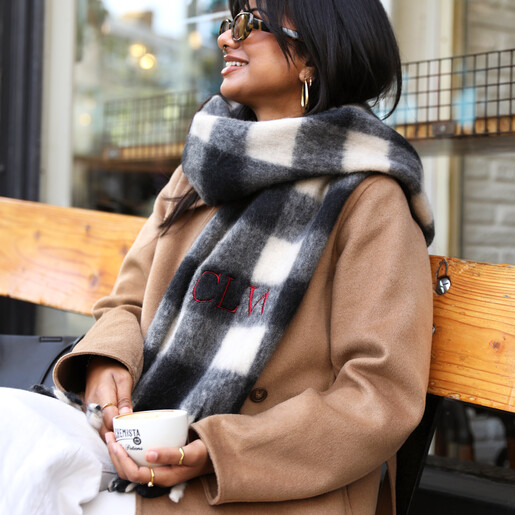 Model wearing a personalised black and white check winter scarf with red embroidered initials.