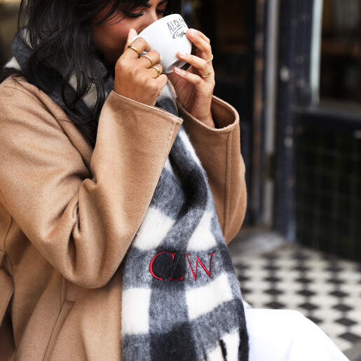 Model holding a warm drink while wearing the personalised black and white check scarf.