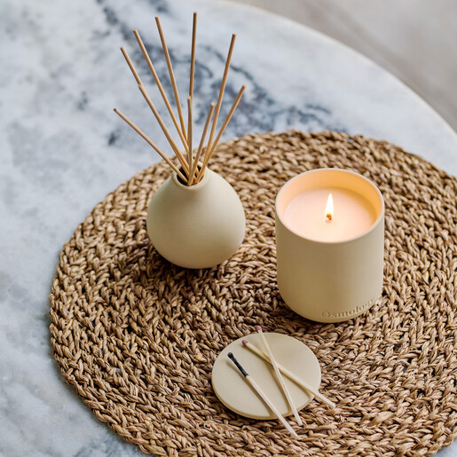Osmology reed diffuser displayed on a woven mat with matching candle and matches
