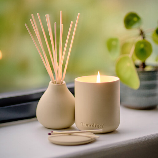 Osmology diffuser and lit scented candle styled on a sunny windowsill next to a houseplant