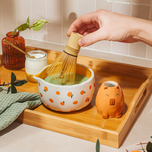 Whisking green matcha tea in orange patterned ceramic bowl with capybara stand