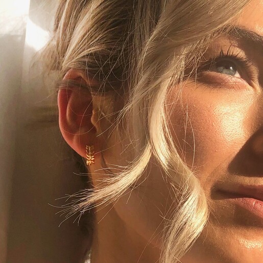 Model is wearing Lisa Angel Fern Leaf Huggie Hoop Earrings in Gold