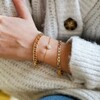 Model Wearing Crystal Daisy Charm Bracelet in Gold Layered with Other Gold Bracelets