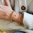 Model Wearing Crystal Daisy Charm Bracelet in Gold Layered with Other Gold Bracelets