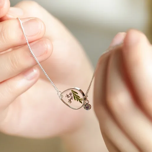 model holding each end of february pressed birth flower charm bracelet with birthstone