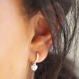 Close Up of Polished Heart Huggie Hoop Earrings in Silver on Model