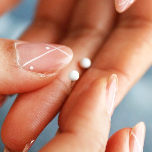 model holding White Ball Stud Earrings in Gold between their fingers
