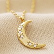 Close Up of Crystal Crescent Moon Necklace in Gold on Beige Fabric