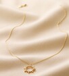 Full Length Shot of Crystal Sunburst Pendant Necklace in Gold on Fabric