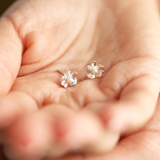 Model holding small Estella Bartlett Silver Pearl Buttercup Stud Earrings