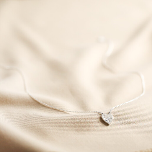 Full chain length of Estella Bartlett Love Engraved Heart Pendant Necklace on fabric background