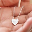 Model Holding Estella Bartlett Love Engraved Heart Pendant Necklace in palm of their hand