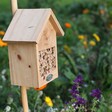 Wooden Bee House Hanging on Garden Post with Flowers in Background