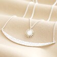 Close Up of Sun and Horn Layered Necklace in Silver on Beige Fabric