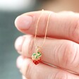Model Holding Tiny Strawberry Charm Necklace in Gold