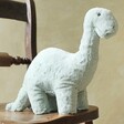 Jellycat Fossilly Brontosaurus Soft Toy sat on wooden chair