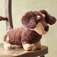 Jellycat Otto Sausage Dog Soft Toy sat on wooden chair