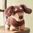 Jellycat Otto Sausage Dog Soft Toy facing camera sat on wooden chair