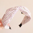 front of Purple Polka Dot Twist Fabric Headband held in front of pink backdrop