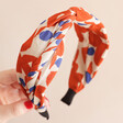 Twist Fabric Headband in Orange and White in front of pink backdrop