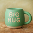 Sass & Belle Big Hug Mug in Green standing on wooden table in front of green background