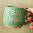 model holding Sass & Belle Big Hug Mug in Green by the handle in front of a green background