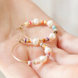 Model Holding Colourful Bead and Pearl Hoop Earrings in Gold