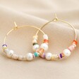Colourful Bead and Pearl Hoop Earrings in Gold on Beige Fabric