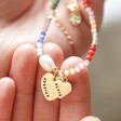 model holding personalised rainbow beads and freshwater pearl necklace with two charms in hand