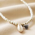 Close Up of White Beaded Shell Charm Necklace on Beige Fabric