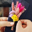 Model Holding Rainbow Brights Dried Flower Buttonhole Against Navy Lapel