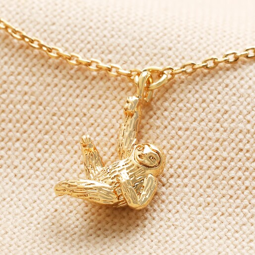 Close up of Hanging Sloth Bracelet in Gold on beige fabric