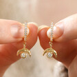 Model Holding Crystal Crescent Moon Huggie Earrings in Gold in Between Fingers