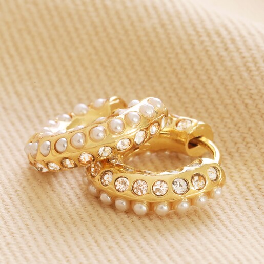 Crystal and Pearl Huggie Hoop Earrings in Gold Laid Out on Neutral Coloured Fabric