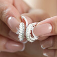 Model Holding Crystal and Pearl Huggie Hoop Earrings in Silver Between Fingers